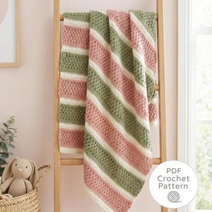 May include: A handmade crochet blanket in shades of pink, green, and white, draped over a wooden ladder. The blanket features diagonal stripes and a textured stitch pattern. A basket with a stuffed bunny is in the foreground. The image includes a "PDF Crochet Pattern" graphic.