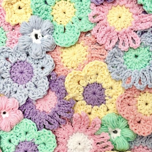 Puede incluir: Primer plano de una colecci&oacute;n de flores de ganchillo coloridas. Las flores son de varios colores pastel, incluyendo rosa, amarillo, azul, verde y morado. El trabajo de ganchillo es detallado, con cada flor teniendo un dise&ntilde;o de p&eacute;talo distinto.