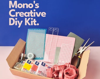 May include: A brown cardboard box filled with a variety of craft supplies, including polymer clay, cutters, a ruler, a stencil, and pliers. The box is open and the supplies are visible. The text "Mono's Creative DIY Kit." is printed on a blue background.