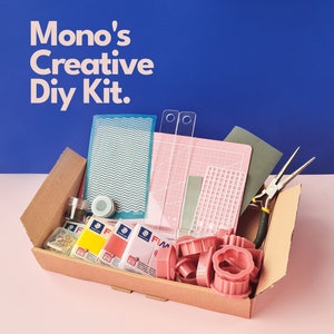 May include: A brown cardboard box filled with a variety of craft supplies, including polymer clay, cutters, a ruler, a stencil, and pliers. The box is open and the supplies are visible. The text "Mono's Creative DIY Kit." is printed on a blue background.