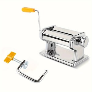 Puede incluir: Una máquina de pasta de plata con un mango amarillo y un accesorio de abrazadera. La máquina de pasta tiene una manivela y un rodillo para hacer láminas de pasta.