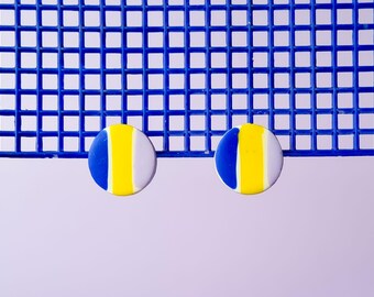 May include: A pair of round earrings with a blue, yellow, and white striped design. The earrings are on a blue grid background.