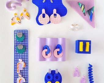 Peut inclure: Assortiment de boucles d'oreilles en argile polymère colorées présentées sur des fonds bleus et violets. Les boucles d'oreilles présentent des formes géométriques, des motifs abstraits et des volutes.