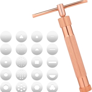 Könnte beinhalten: Eine roségoldene Keksform mit 16 austauschbaren Scheibenspitzen. Die Spitzen umfassen verschiedene Formen wie Kreise, Quadrate, Dreiecke und Sterne.