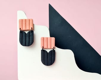 May include: A pair of black and coral pink geometric earrings. The earrings are made of polymer clay and have a modern, abstract design.