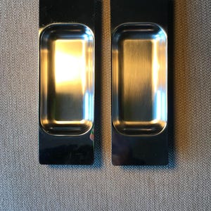 May include: Two silver rectangular cabinet door pulls with a recessed centre.