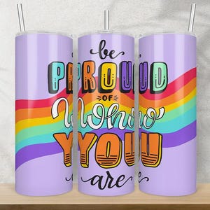 Pode incluir: Três copos de aço inoxidável com um design de arco-íris e o texto "be proud of who you are".