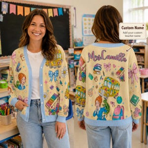 Op de afbeelding: Een crèmekleurig vest met een lichtblauwe bies voorzien van een herhalend patroon van schoolbussen, boeken, xylofoons, strikken, madeliefjes en een cartoonlerares met een hagedis. De achterkant toont de tekst Mrs. Camilla in cursief schrift.