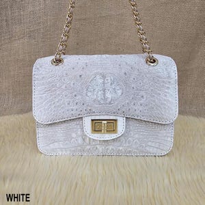 May include: White handbag with a textured, crocodile-like pattern. The bag features a gold chain strap and a gold clasp closure. The word "WHITE" is printed at the bottom of the image.