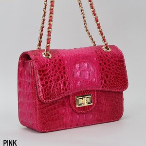 May include: A pink handbag with a textured, crocodile-like pattern. The bag has a gold chain strap and a gold clasp closure. The word "PINK" is printed at the bottom left corner of the image.