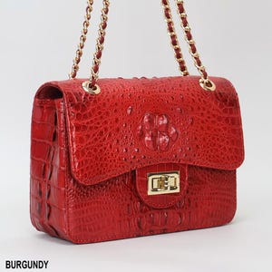 May include: Burgundy-colored handbag with a textured crocodile-like pattern. The bag features a gold-tone clasp and chain strap. The word "BURGUNDY" is printed at the bottom of the image.