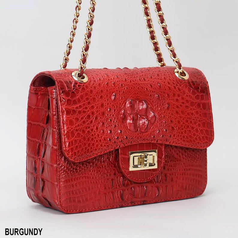 May include: Burgundy-colored handbag with a textured crocodile-like pattern. The bag features a gold-tone clasp and chain strap. The word "BURGUNDY" is printed at the bottom of the image.