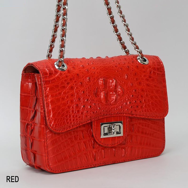 May include: A red handbag with a textured, crocodile-like pattern. The bag has a silver chain strap and a silver clasp closure. The word "RED" is printed in the bottom left corner.