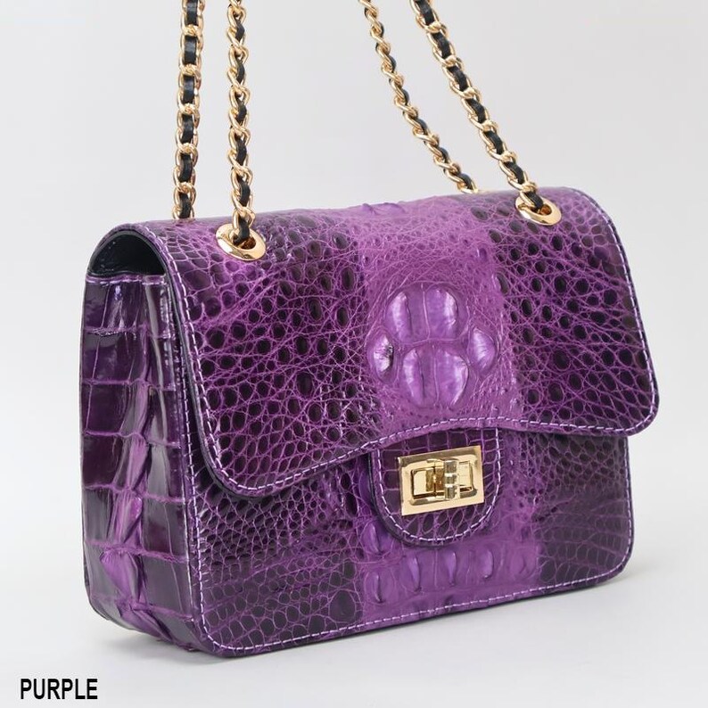May include: A purple handbag with a textured, crocodile-like pattern. The bag features a gold chain strap and a gold clasp closure. The word "PURPLE" is printed at the bottom of the image.