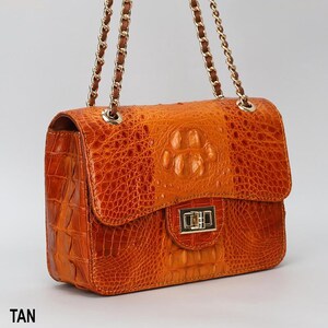 May include: Tan leather handbag with a textured crocodile pattern. The bag features a flap closure with a gold-tone clasp and chain straps. The word "TAN" is printed at the bottom of the image.