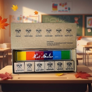 Könnte beinhalten: Eine Box mit farbigen Stempelkissen und Stempeln steht auf einem Schreibtisch in der Schule. Die Stempelkissen sind in einem Regenbogenspektrum angeordnet, mit dem Text "Let's Color" auf der Vorderseite. Die Stempel haben eine Cartoonfigur und deutschen Text.