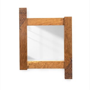 May include: A wooden frame mirror with a decorative pattern on the edges. The frame is made of light brown wood with a natural finish.