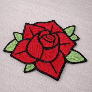 May include: Embroidered red rose patch with black edging and green leaves. The rose is a classic floral design, suitable for adding to clothing or accessories. The patch is a vibrant, eye-catching accessory.