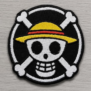 Peut inclure: Un écusson brodé circulaire représentant un crâne blanc portant un chapeau de paille jaune avec une bande rouge. Le crâne est centré sur un fond noir, entouré d'une bordure circulaire blanche et de deux os blancs croisés derrière le crâne.