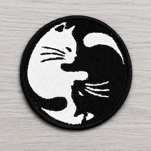 Könnte beinhalten: Ein runder bestickter Aufnäher mit einem schwarz-weißen Design einer Katze, die sich in Yin-Yang-Form zusammenrollt. Die weiße Katze nimmt die linke Seite ein, wobei ihr Schwanz in den schwarzen Bereich ragt, der den Körper der Katze bildet.