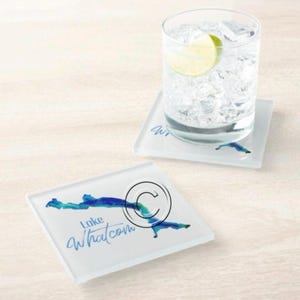Könnte beinhalten: Zwei quadratische Glasuntersetzer mit einem blau-türkisfarbenen Aquarelldesign eines Sees. Ein Untersetzer hat ein Glas Wasser mit Eis und einer Limettenscheibe. Der Text "Lake Whatcom" ist auf einem Untersetzer aufgedruckt.