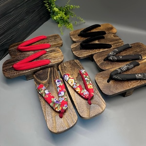 May include: Wooden geta sandals with various strap designs. The sandals feature dark wood platforms and fabric straps in red, black, and floral patterns. The geta are a traditional Japanese footwear style, often worn with a kimono.