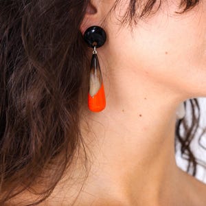 Peut inclure: Boucles d'oreilles pendantes avec un clou noir et une goutte en forme de goutte. La breloque présente un dégradé de couleurs, passant du marron au blanc et se terminant par une pointe orange vif. Bijou audacieux.