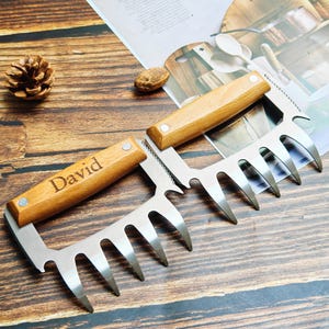 May include: Two stainless steel meat shredder claws with wooden handles. One handle is engraved with the name "David". The claws have sharp, pointed tines for easy shredding of cooked meats. Perfect for barbecue enthusiasts.