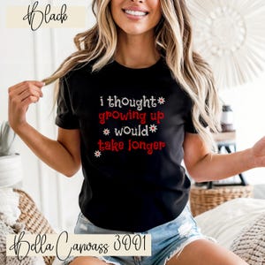 Puede incluir: Camiseta negra con el texto blanco y rojo "i thought growing up would take longer". La camiseta también tiene el texto "Bella Canvas 3001".
