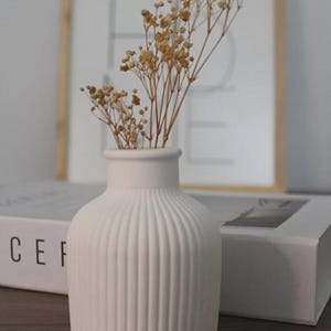 May include: A white ceramic mug with a black handle and the text "But First, Coffee" in a black, handwritten-style font. The mug is on a white surface.