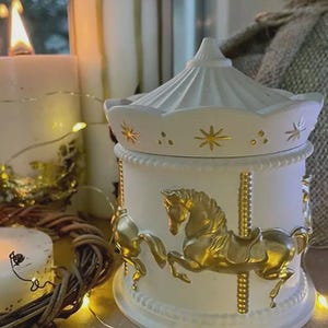 May include: White carousel-style decorative jar with gold detailing. The jar showcases a carousel horse design and a domed lid with star motifs. Lit candles and fairy lights create a warm atmosphere.