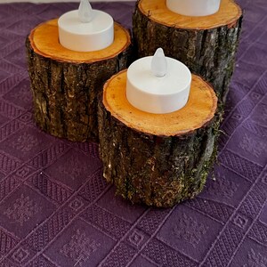 Puede incluir: Tres portavelas de madera con un acabado natural de corteza. Cada portavelas tiene una pequeña vela LED de té blanca en su interior.