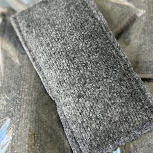 May include: A rectangular cleaning sponge featuring a textured, dark gray abrasive surface. The sponge has a dense, looped fiber construction with stitched edges, designed for scrubbing tasks, and is individually wrapped in clear plastic packaging.