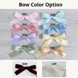 A collection of nine decorative bows labeled with codes RB1 through RB8 and LB9. The bows include satin finishes in light pink, dusty rose, lavender, sage green, light blue, cornflower blue, pale yellow, and tan, plus one cream lace bow.