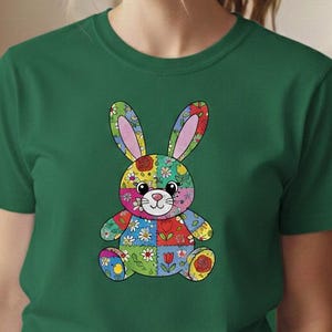 Puede incluir: Una camiseta verde con un diseño de conejo de patchwork colorido. El conejo está compuesto por varios patrones florales y geométricos en tonos de rojo, amarillo, azul y verde. La camiseta es de manga corta y tiene cuello redondo.