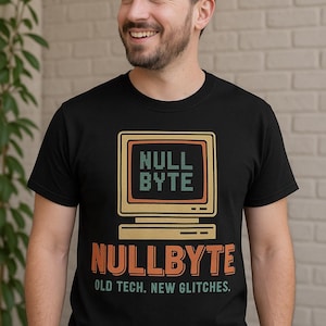 Puede incluir: Camiseta negra con un gráfico de ordenador retro y las palabras "NULL BYTE" en naranja y verde. Debajo del gráfico, el texto "NULLBYTE" y "OLD TECH. NEW GLITCHES." están en la camiseta. La camiseta la lleva una persona sonriente.