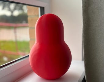 May include: A solid, bright red, pear-shaped decorative object with a smooth, matte finish. The item features a rounded base that tapers upwards into a narrower, rounded top, creating a continuous, seamless silhouette without any visible markings or patterns.