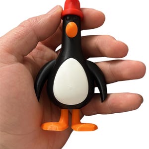 May include: A black and white penguin toy with orange feet and a red hat. The penguin is holding a red and white striped candy cane.
