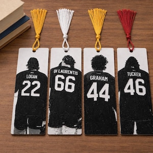 Puede incluir: Cuatro marcap&aacute;ginas rectangulares con im&aacute;genes en blanco y negro de camisetas deportivas vistas desde atr&aacute;s. Las camisetas muestran los nombres Logan 22, Di Laurentis 66, Graham 44 y Tucker 46. Cada marcap&aacute;ginas tiene una borla de tela decorativa en amarillo, blanco, amarillo o rojo.
