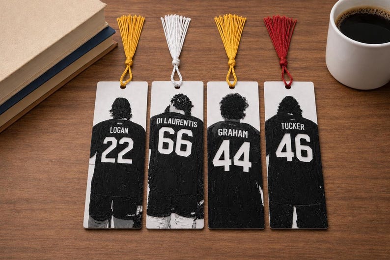 Puede incluir: Cuatro marcap&aacute;ginas rectangulares con im&aacute;genes en blanco y negro de camisetas deportivas vistas desde atr&aacute;s. Las camisetas muestran los nombres Logan 22, Di Laurentis 66, Graham 44 y Tucker 46. Cada marcap&aacute;ginas tiene una borla de tela decorativa en amarillo, blanco, amarillo o rojo.