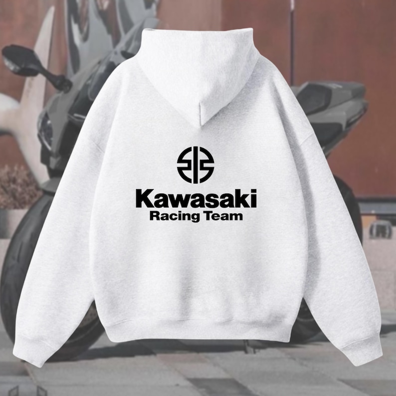 May include: A light gray hoodie featuring the Kawasaki Racing Team logo in black. The logo includes a stylized emblem above the brand name and the words "Racing Team" below. The hoodie has a hood and long sleeves.