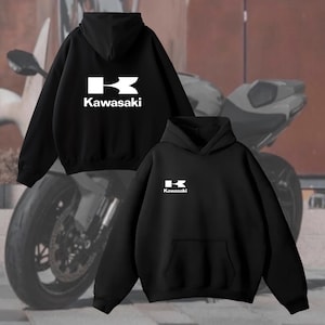 May include: Black hooded sweatshirts with the white Kawasaki logo on the front. The sweatshirts have a kangaroo pocket and a drawstring hood. The background features a motorcycle.