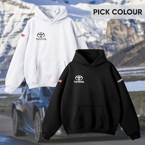 May include: Two hooded sweatshirts, one white and one black, featuring the Toyota logo and text. The white sweatshirt has a red and black GR logo on the sleeve. The black sweatshirt has a white Toyota logo. The text "PICK COLOUR" is at the top.