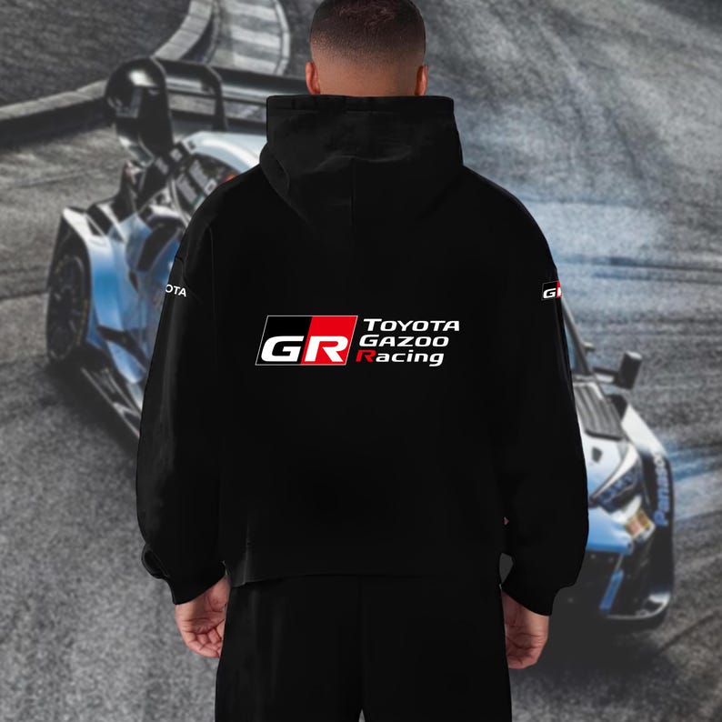 May include: Black hooded sweatshirt with the "GR Toyota Gazoo Racing" logo in white, red, and black. The sweatshirt has a drawstring hood and a front pocket. A race car is in the background.
