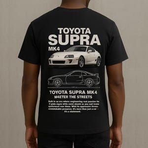 Könnte beinhalten: Schwarzes T-Shirt mit einem weißen Aufdruck eines Toyota Supra MK4. Die Grafik enthält den Namen des Autos, die Modellnummer und eine Strichzeichnung des Autos. Der Text "M4ETER THE STREETS" ist ebenfalls auf der Grafik enthalten.