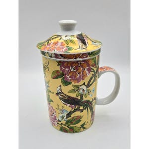 Puede incluir: Una taza de cerámica blanca con un asa negra y el texto "But First, Coffee" en un estilo manuscrito. La taza está sobre una superficie blanca. La taza mide aproximadamente 10 cm de alto.
