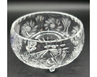 Peut inclure: Un bol en verre taillé transparent, de forme arrondie et doté de trois petits pieds. Le bol présente des motifs complexes d'éclats d'étoiles et de fleurs gravés dans le verre, créant un effet scintillant. Idéal pour servir ou exposer.