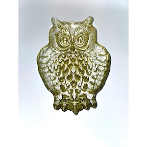 May include: A decorative owl figurine in a golden-yellow hue. The owl has large, detailed eyes and textured feathers. The figurine is made of a translucent material, and the design is visible from the front.