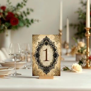 May include: A rectangular table number card featuring the digit 1 in a dark brown serif font. The card has a beige, parchment-like background with a black, ornate, filigree-style frame surrounding the number and decorative floral patterns.