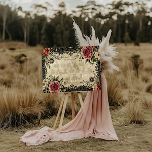 May include: A rectangular wedding seating plan sign featuring a vintage parchment-style background, black ornate lace-like borders, and large red and pink floral illustrations. The text reads Sarah & Jack The Seating Plan with tables 1 through 15.